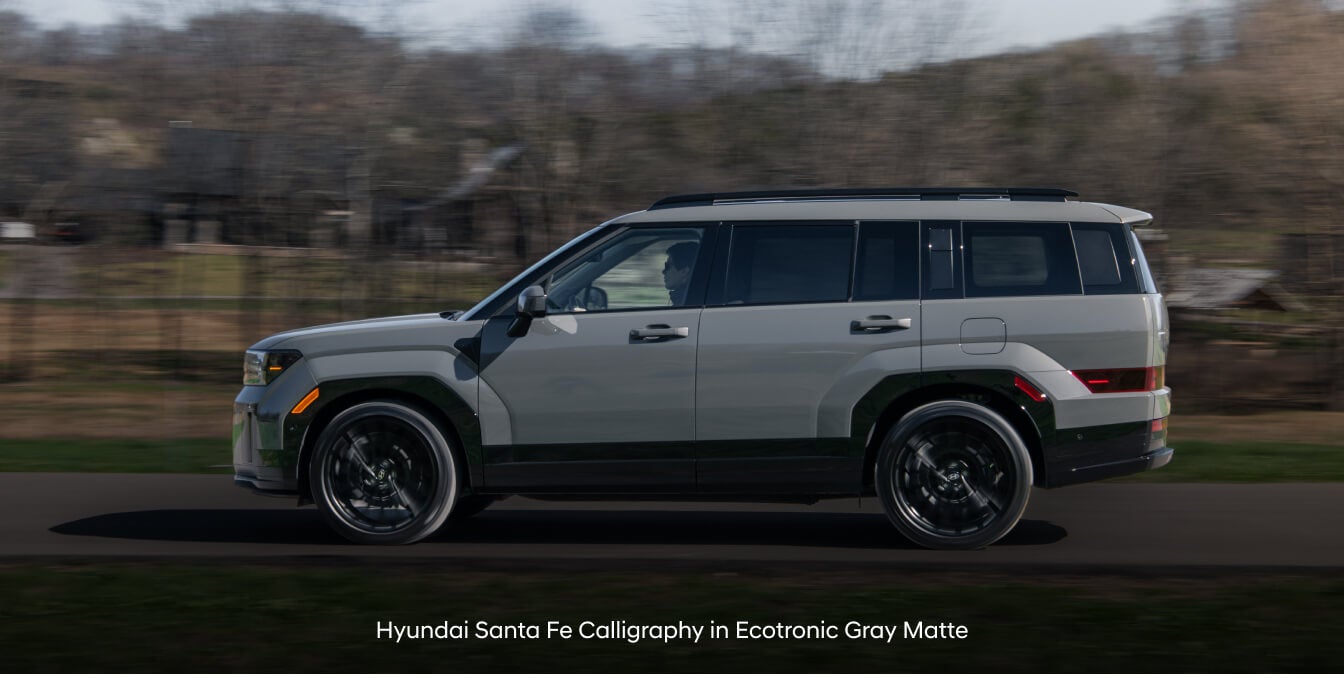 Hyundai Santa Fe Calligraphy in Ecotronic Gray Matte with roof side rails on paved road.