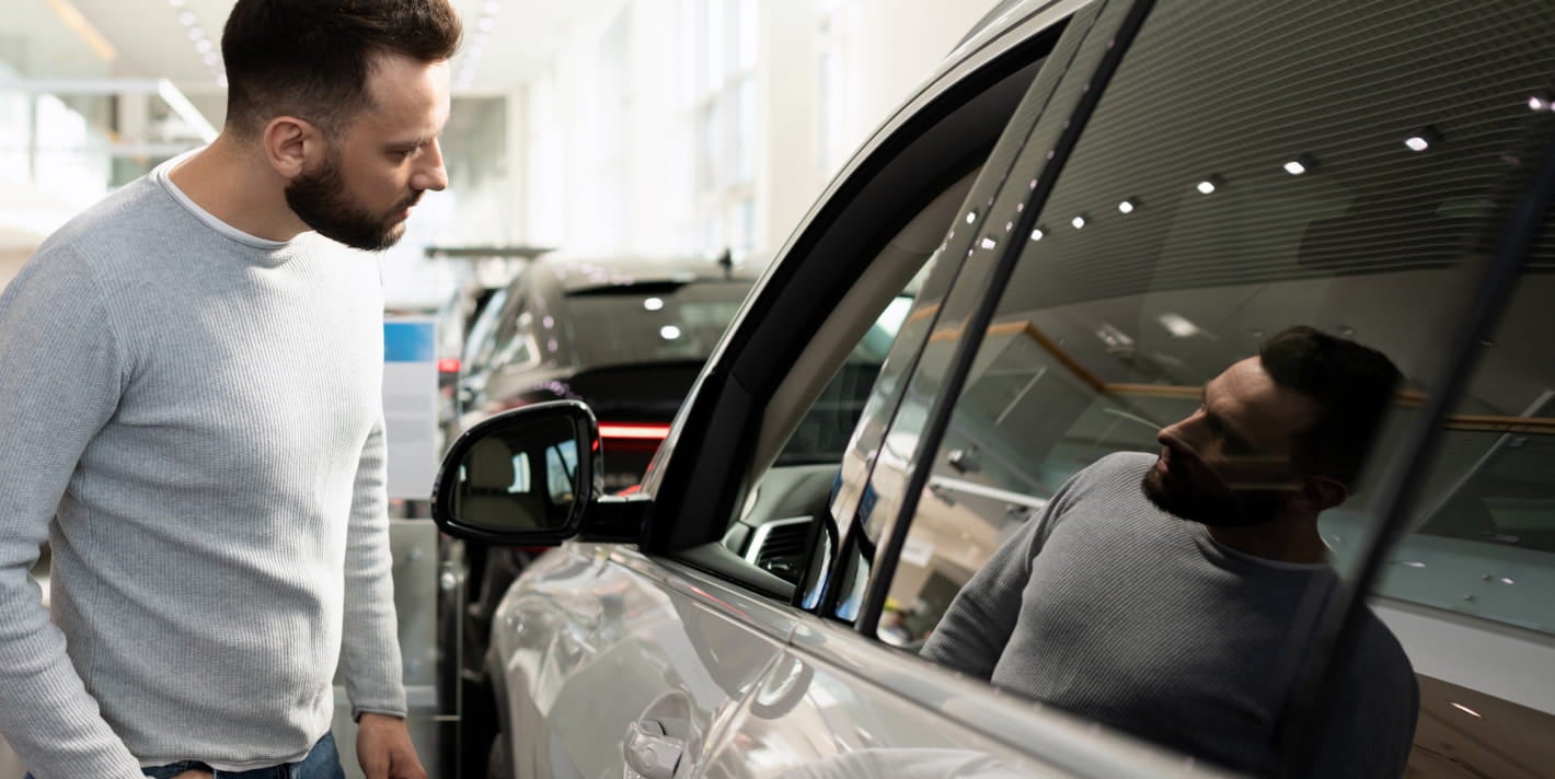 Customer examining the exterior of a vehicle inside a car dealership showroom.