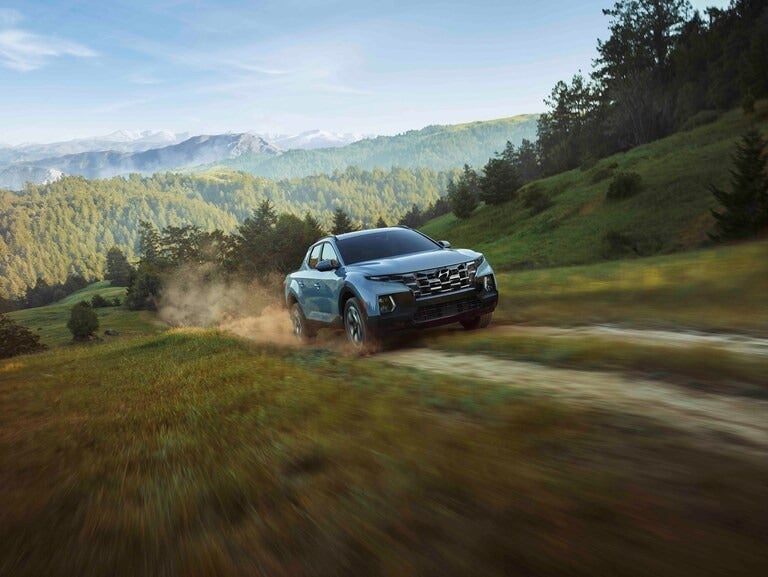 Hyundai Santa Cruz moving quickly down dirt road in a forest clearing