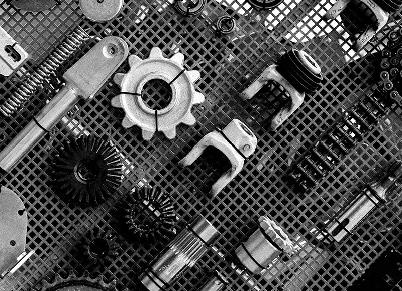 A black-and-white photograph showing various metal machine components arranged on a metal mesh surface